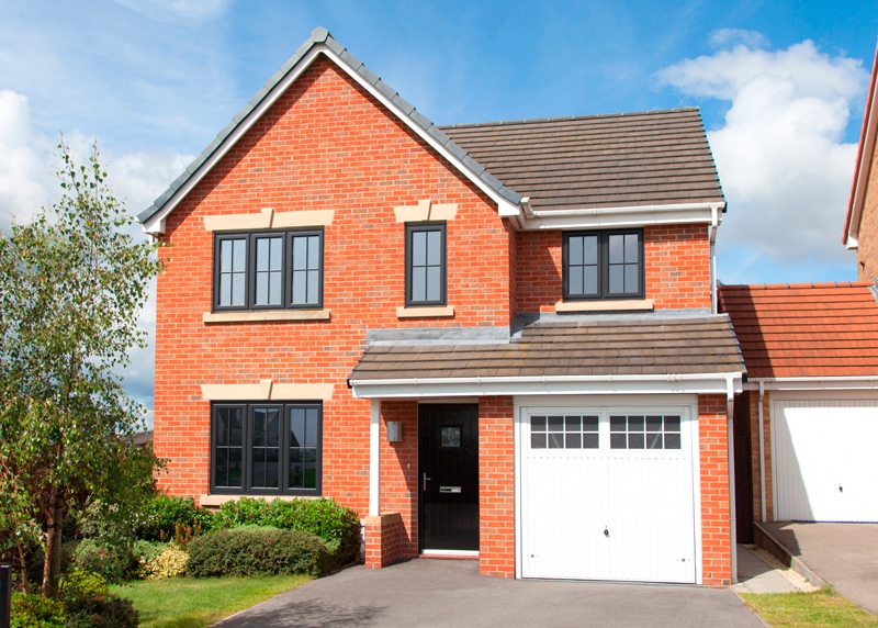 Red brick house with black casement windows and a white garage door, set against a clear blue sky.